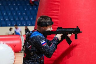 Игрок LASERWAR целится из-за красного надувного препятствия.